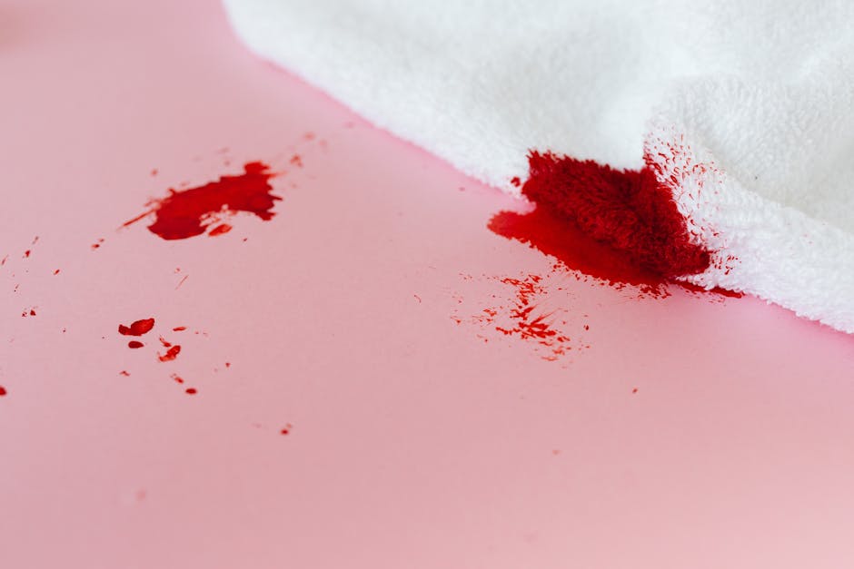 Close-up view of a kitchen countertop with a scattering of white flour and small spills around a partially visible white mug, a metal spoon, and a plate with a slice of toast spread with jam. The surf